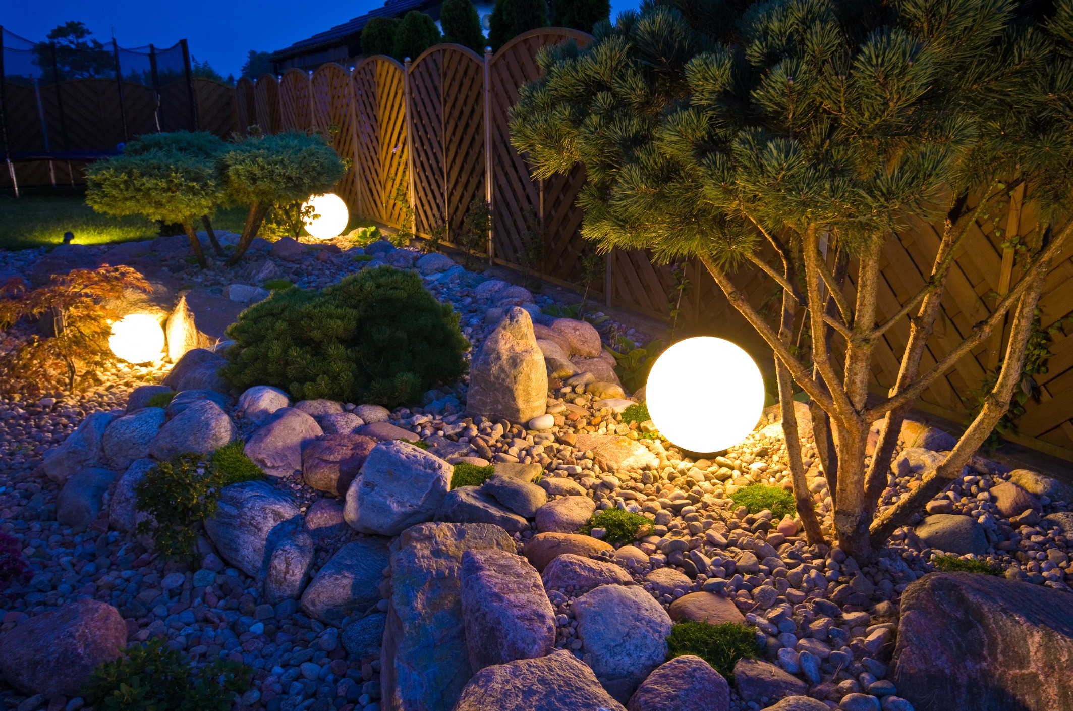 Illuminated garden scene with glowing spherical lights, rocks, and trees at night, creating a serene and peaceful atmosphere. No people or landmarks visible.