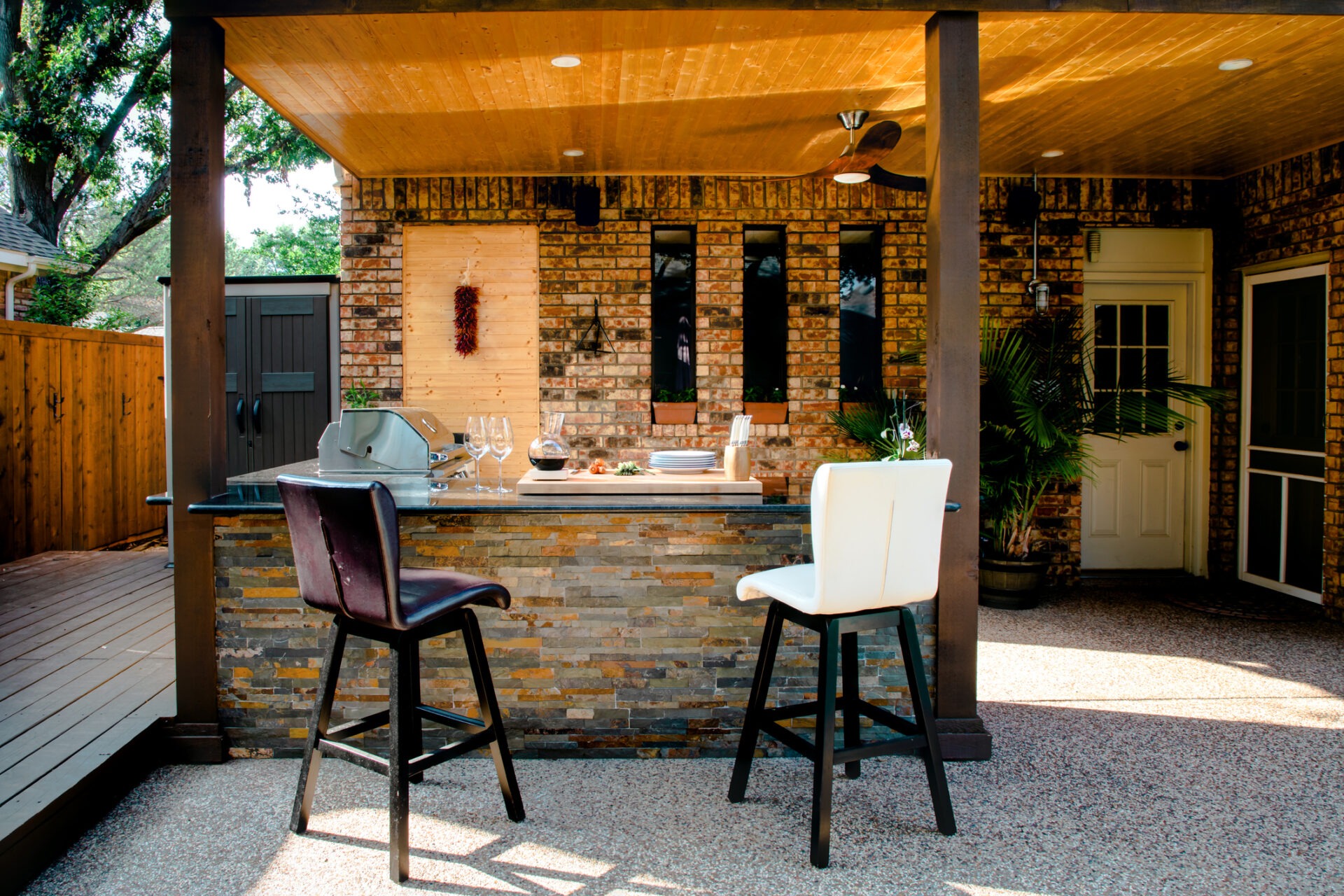 Outdoor patio with brick walls, two bar stools, and a bar counter. There are plants and a grill in the cozy setup.