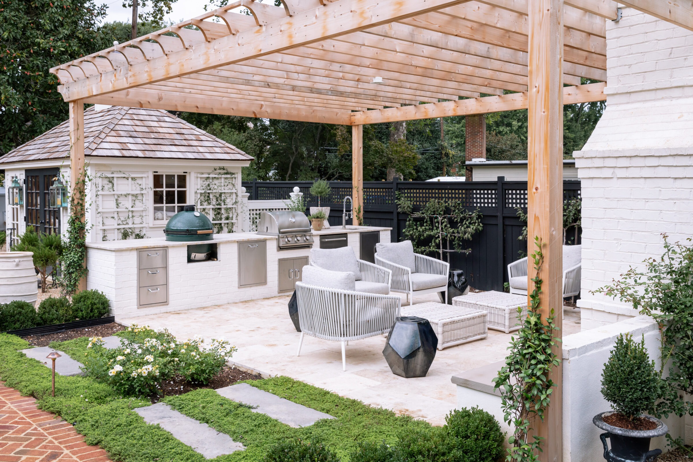 Elegant outdoor patio with a pergola, comfortable seating, brick path, and a modern outdoor kitchen featuring a grill and decorative greenery.