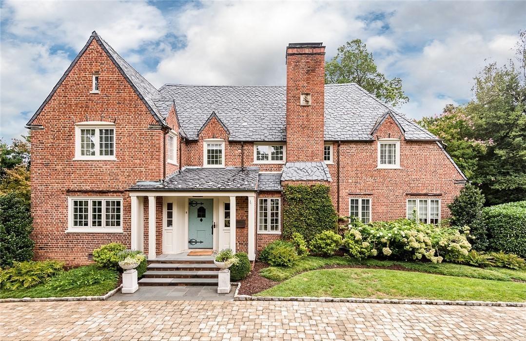 Brick estate home with manicured lawn, foundation plantings, and stone driveway