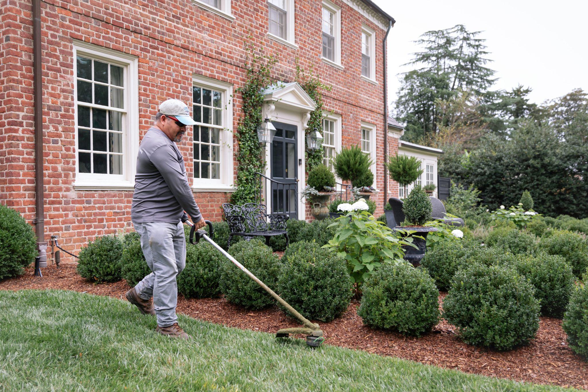 Landscaping professional trimming garden bed in front of brick estate home